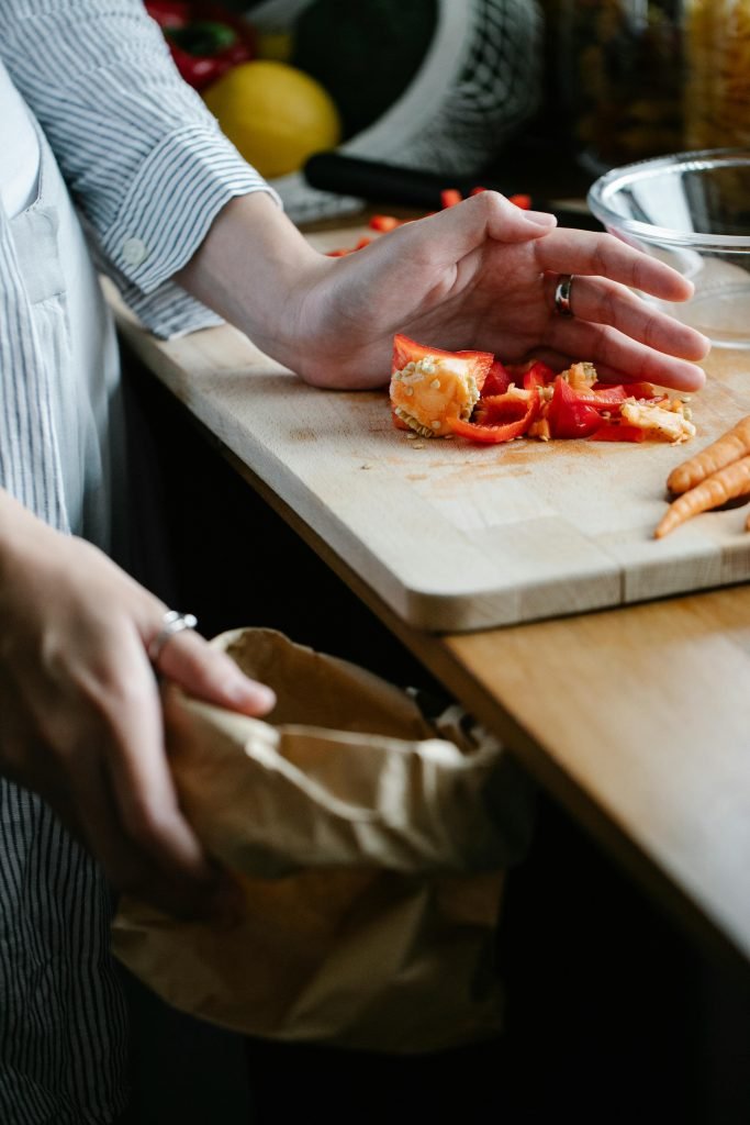 pexels-photo-7262910-7262910 Crop anonymous housewife throwing vegetable leftovers on chopping board while cooking in light kitchen